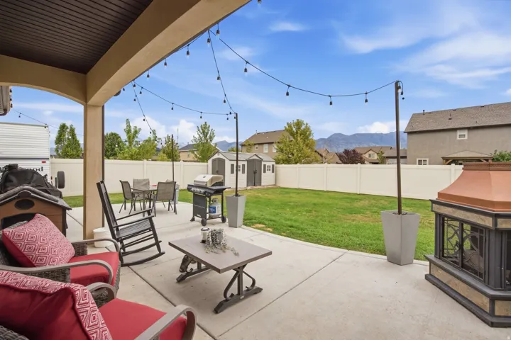 Covered concrete patio with an outdoor fireplace, string lighting, and a fenced backyard