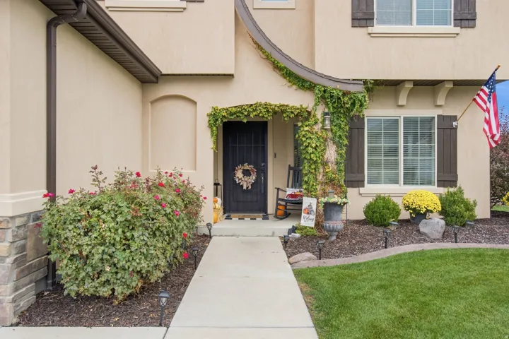 Stucco exterior with stone accent, dark wood window shutters, a covered entry, and a concrete walkway