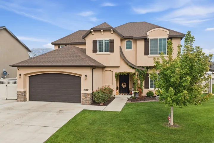 Stucco exterior with stone accents, arched garage door, dark window shutters, gabled roof, and a manicured lawn