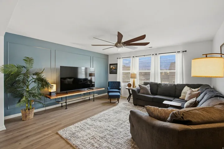 Accent wall with panel molding, wood-finish flooring, ceiling fan with wood-tone blades, multiple windows with blinds, and recessed lighting
