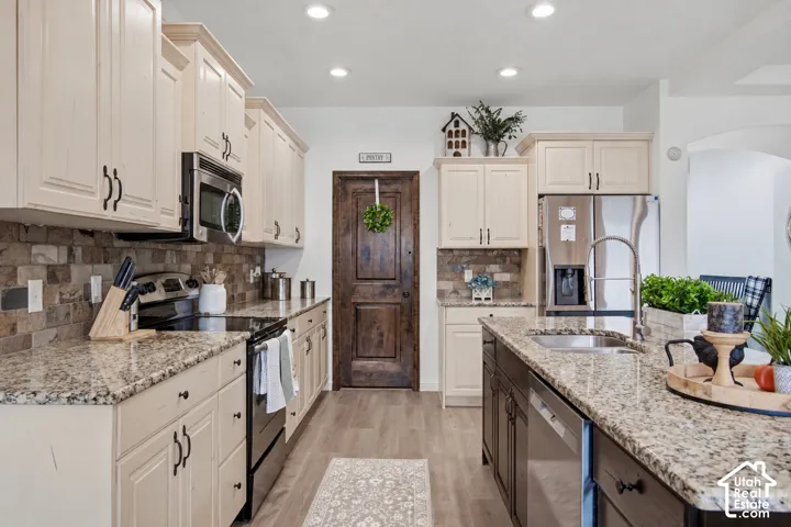 Kitchen featuring stone tile backsplash, light-toned cabinetry, stainless steel appliances, and granite countertops
