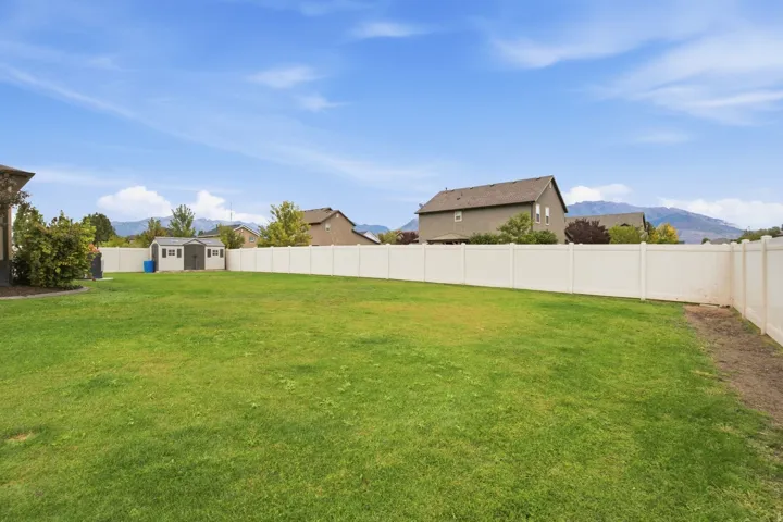 Expansive lawn area with a white vinyl fence and a detached storage shed