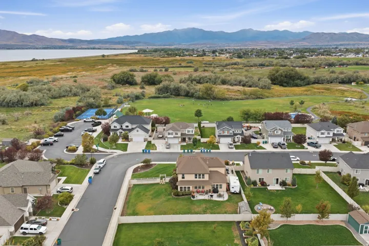 Residential neighborhood featuring a paved street, manicured lawns, and a distant lake and mountains