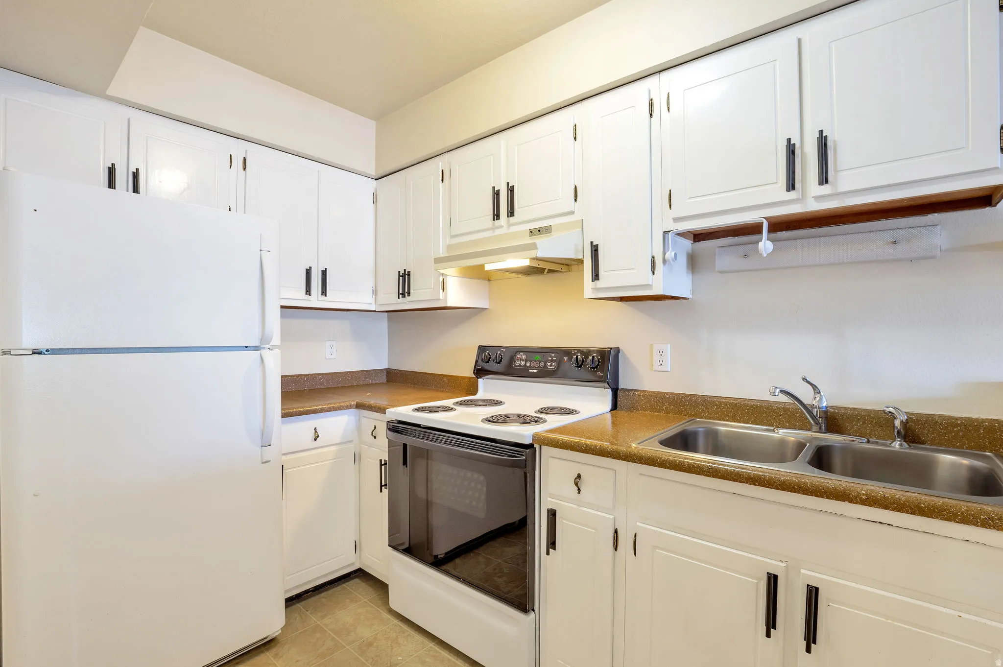 Kitchen Featuring White Cabinetry, a White Top-Freezer Refrigerator, a White Electric Range, and a Stainless Steel Double Basin Sink