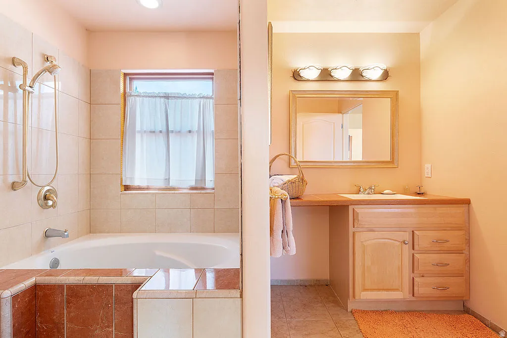 Bathroom featuring a built-in tub, tiled surround, window, wood-finish vanity with an integrated sink, and an overhead light fixture