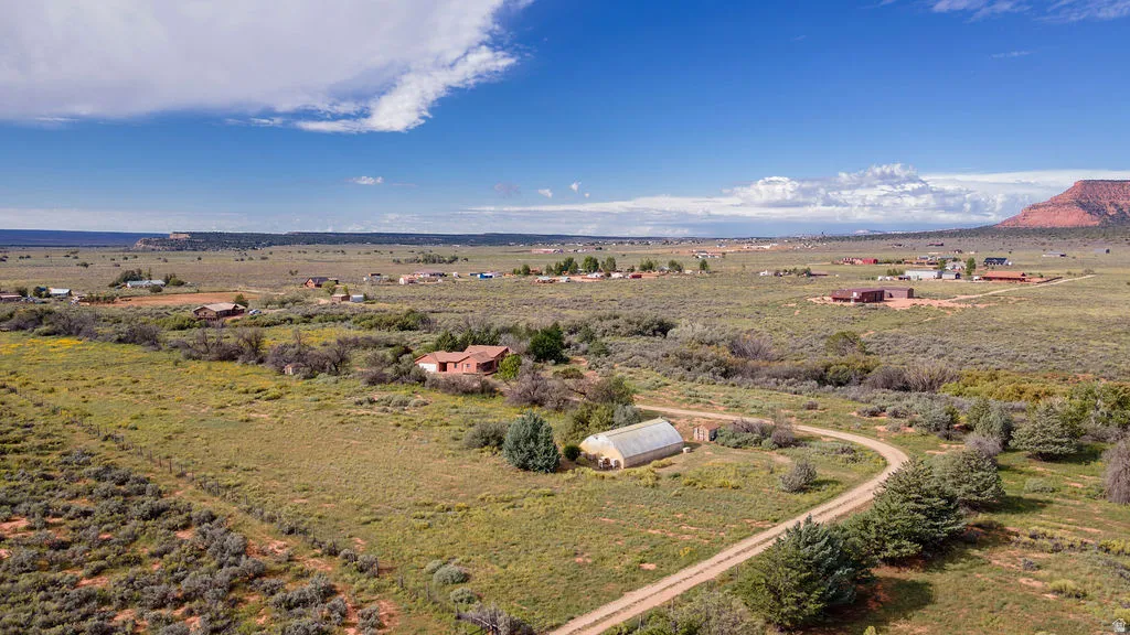 Scenic rural acreage featuring expansive green pastureland, mature tree clusters throughout the property, a curved driveway approach, and distant mountain backdrop