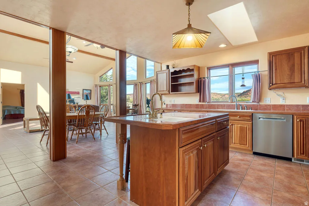 Spacious kitchen featuring a large wood-finish island with storage and seating, wood cabinetry throughout, stainless steel appliances, tile flooring, and abundant natural light from multiple windows and skylights