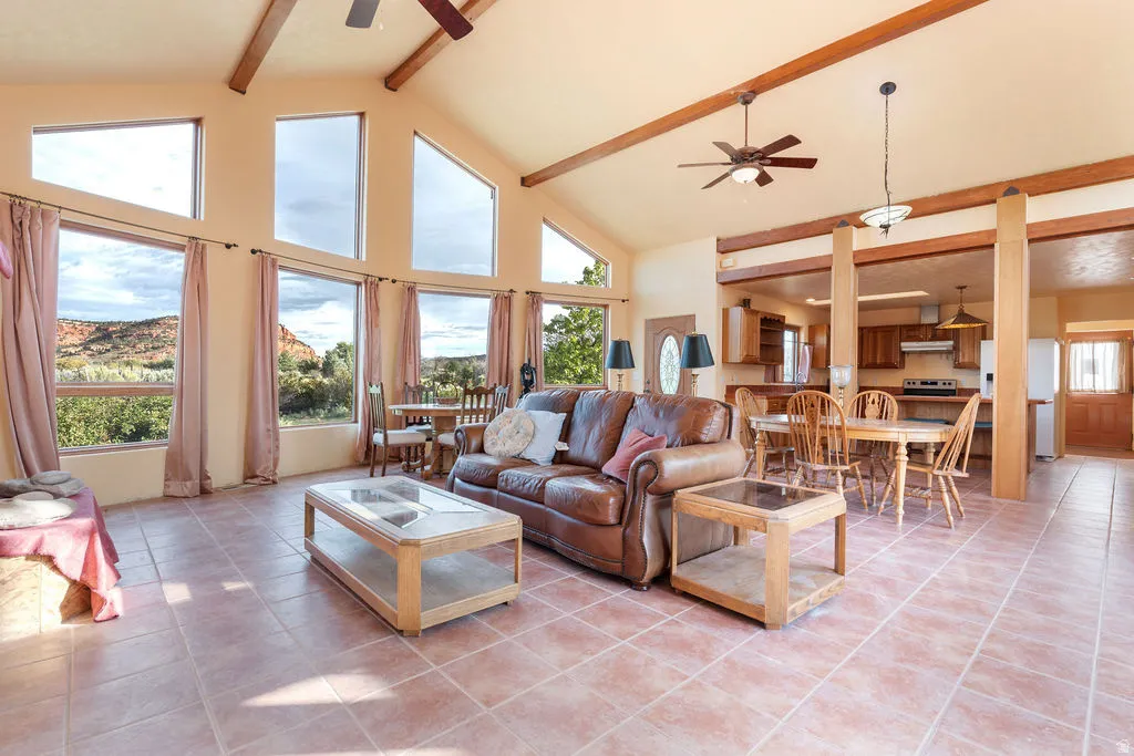 Vaulted ceiling with exposed wood beams, expansive floor-to-ceiling windows, tile flooring, and integrated kitchen/dining areas