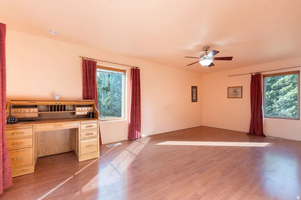 Expansive interior space featuring wood-finish flooring, two large windows, and a ceiling fan