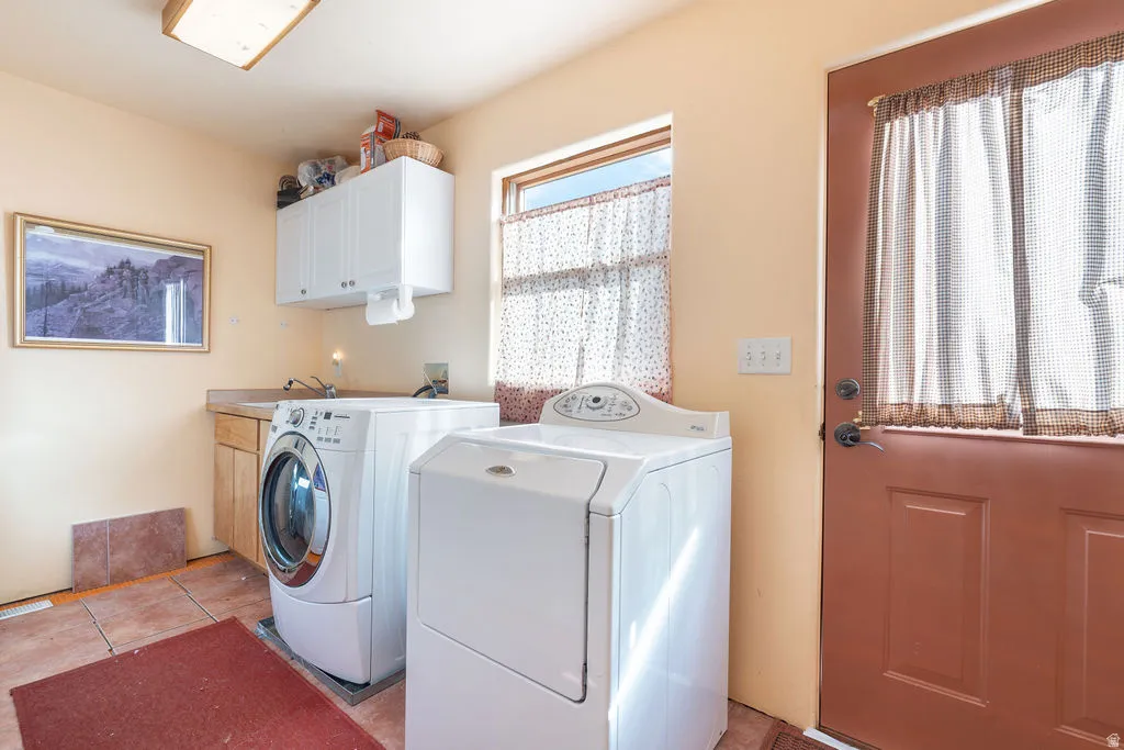 Laundry area featuring a utility sink, wood-finish base cabinetry, white upper cabinets, and tile flooring