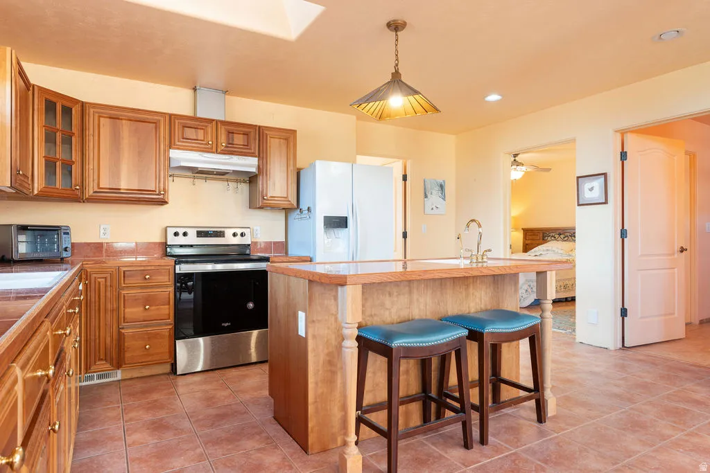 Kitchen featuring wood cabinetry, stainless steel oven, tiled flooring, island with sink, and recessed lighting