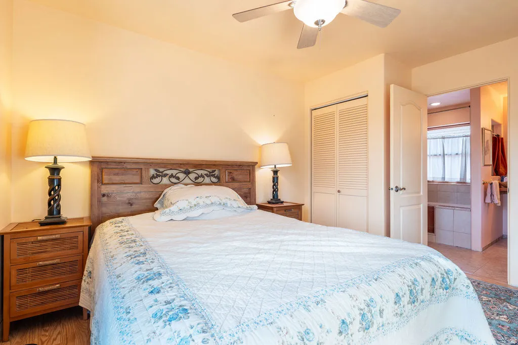 Wood-finish flooring, ceiling fan with integrated lighting, louvered bi-fold closet doors, and an en-suite bathroom entrance