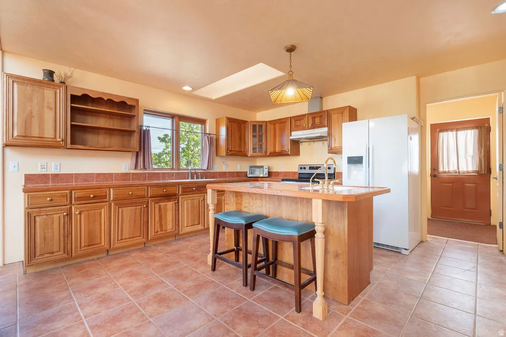 Wood cabinetry, tile flooring, central island, skylight, and pendant lighting