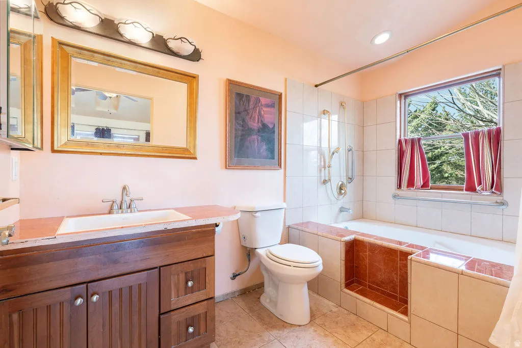 Bathroom featuring a wood-finish vanity with a single basin sink, gold-framed mirror, and a tiled bathtub surround with an integrated shelf