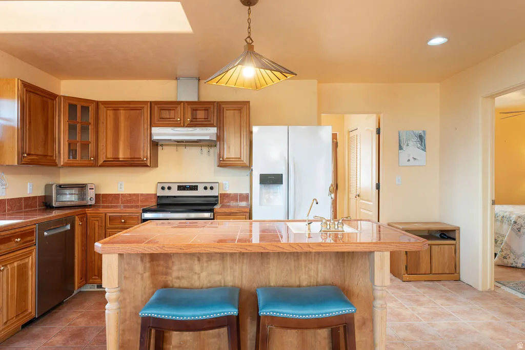 Kitchen featuring wood cabinetry, stainless steel dishwasher, electric range, and a center island with a tile countertop