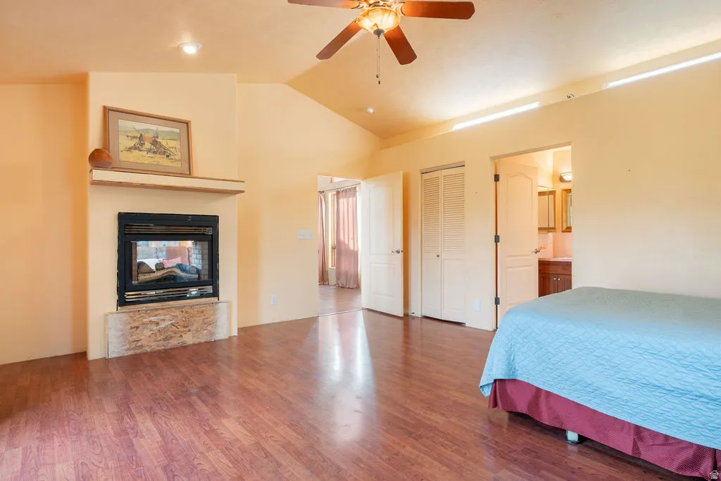 Vaulted ceiling with a ceiling fan, fireplace with a mantel, wood-finish flooring, and bi-fold closet doors