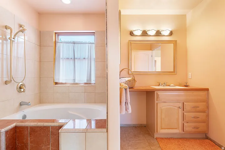 Bathroom featuring a built-in tub, tiled surround, window, wood-finish vanity with an integrated sink, and an overhead light fixture