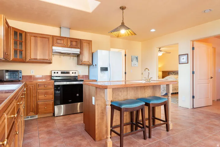 Kitchen featuring wood cabinetry, stainless steel oven, tiled flooring, island with sink, and recessed lighting