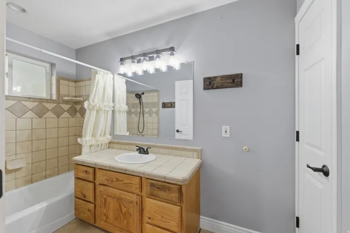 Master Bathroom featuring a wood-finish vanity with a tiled countertop, a built-in bathtub with tiled surround, and a wall-mounted light fixture