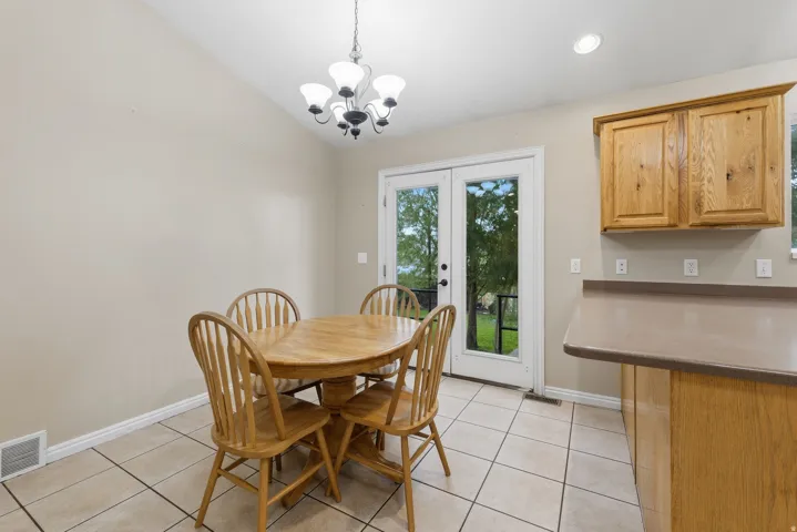 Bright dining area with ceramic tile flooring, round wood pedestal table, Windsor-style chairs, and French doors providing natural light and access to the rear yard