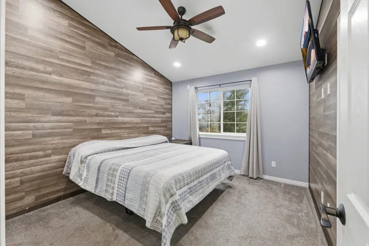 Master bedroom. Vaulted ceiling with a ceiling fan, recessed lighting, wood-finish accent wall, and carpet flooring