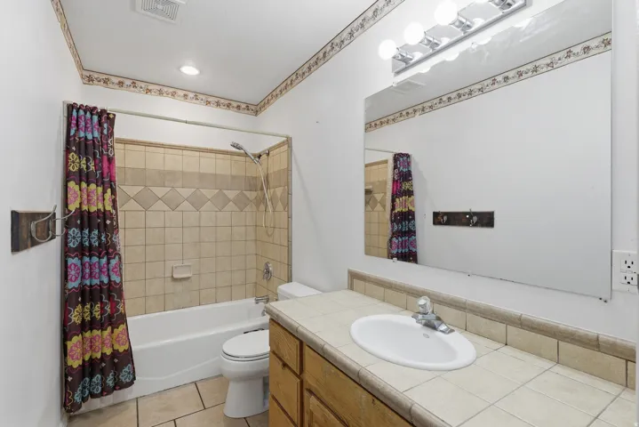 Spacious bathroom featuring a wood-finish vanity with dual sink basins, tile countertop, and ample storage