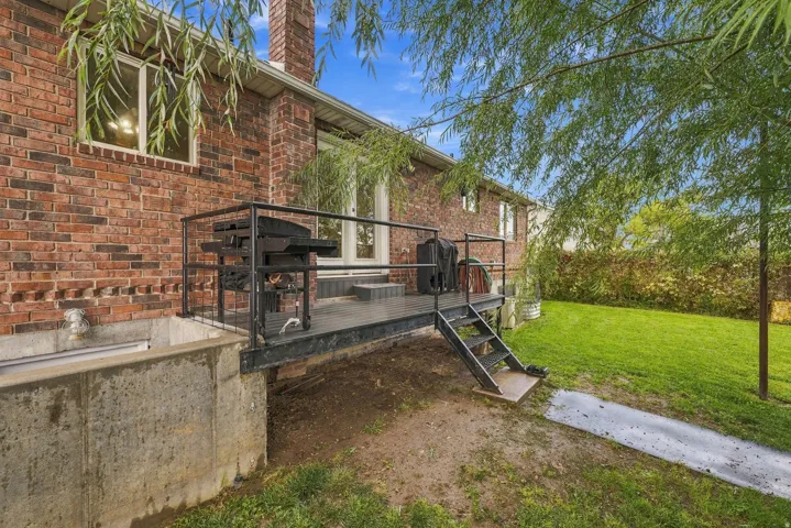 Brick exterior with a prominent chimney, elevated outdoor deck with railings, and a stairway providing access to the grassy yard