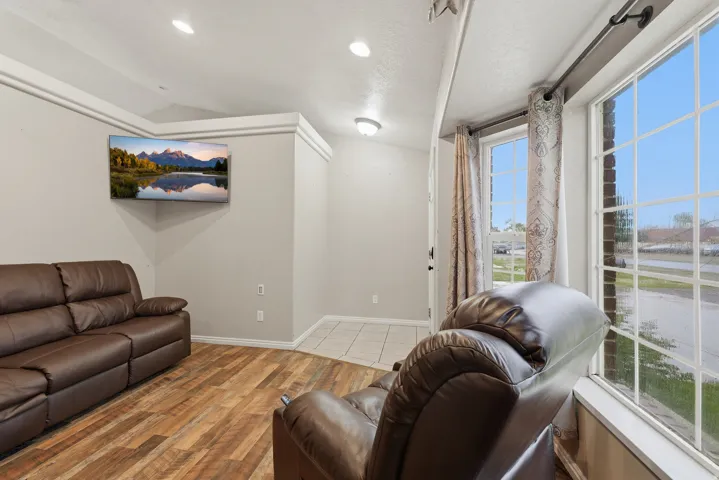 Bright, light-filled living space featuring expansive glass sliding doors with natural sightlines to outdoor grounds, recessed ceiling lighting, wood-finish flooring, and brown leather seating arrangements