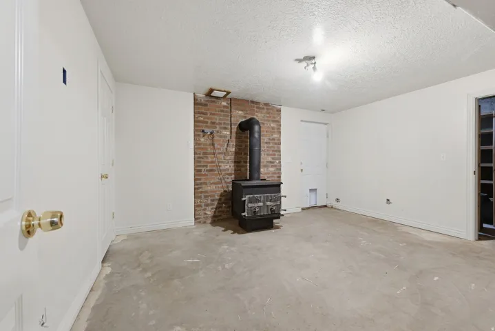 Spacious basement featuring exposed brick chimney with wood-burning stove, concrete flooring, and recessed lighting