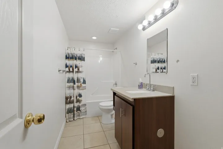 Modern bathroom featuring a dark wood-finish vanity with integrated sink, ceramic tile flooring, and polished brass hardware
