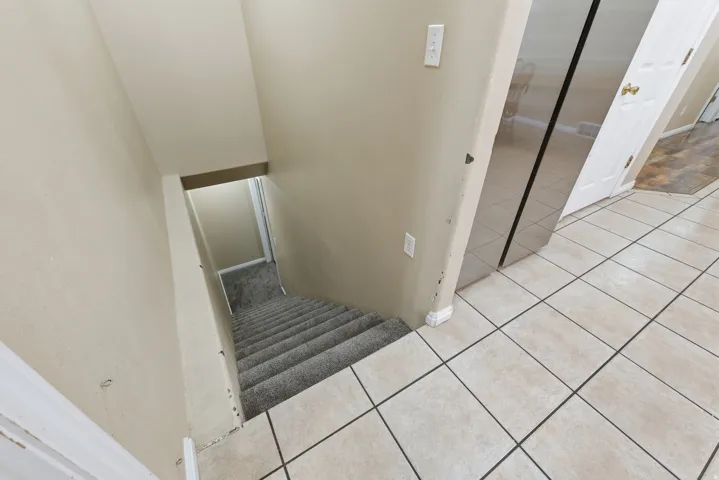 Tiled flooring with dark grout lines, carpeted staircase, and neutral wall paint