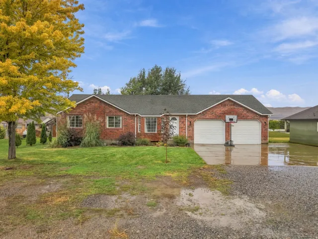 Charming brick ranch home featuring a two-car garage with white panel doors, manicured lawn with mature landscaping, and a gently sloped driveway