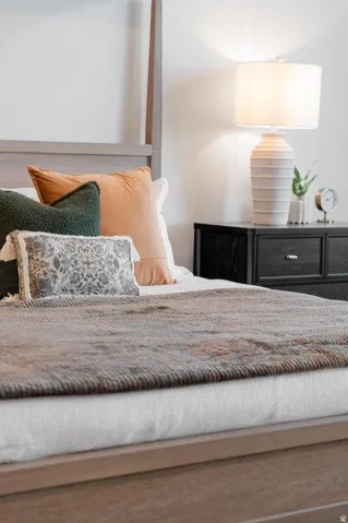Wood-finish flooring with a light-toned bed frame, featuring a dark-toned nightstand with integrated drawers, and a textured ceramic table lamp