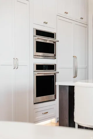 White shaker-style cabinetry with brushed nickel hardware, integrated stainless steel built-in oven, and built-in microwave