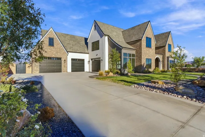 Brick and stucco exterior with multiple gables, three garage bays, arched entry, and a concrete driveway