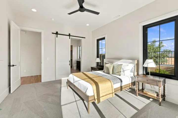 Light-colored walls with recessed lighting, black framed windows, dark ceiling fan, light gray carpet, and a white barn door
