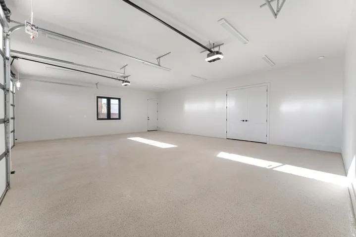 Spacious garage with light-colored epoxy flooring, bright overhead lighting, and white walls