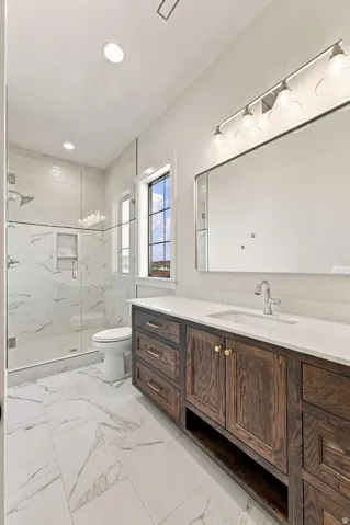 Spacious bathroom featuring a dark wood-finish vanity with an undermount sink, a white countertop, large format tile flooring, and a glass-enclosed shower with tiled walls