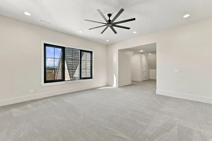 Recessed lighting illuminates this space featuring a ceiling fan, a large window with black framing, and neutral carpeting