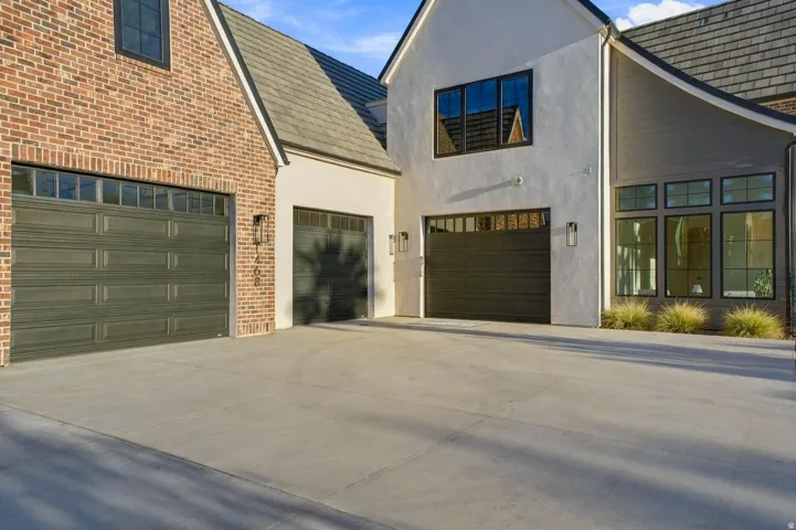 Exterior facade featuring a combination of brick and stucco finishes, multiple garage doors with transom windows, and black-framed windows