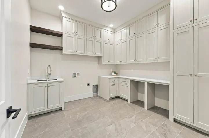 Extensive built-in cabinetry, dual floating wood shelves, integrated sink, light-toned countertop surfaces, and gray tile flooring