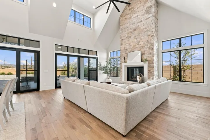 Vaulted ceilings with exposed beams, stone fireplace, wood-finish flooring, and multiple glass panel doors with transom windows