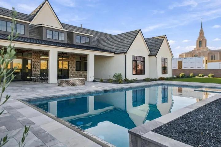 Expansive backyard featuring a rectangular swimming pool, paver patio, covered patio area with brick accents, and a manicured lawn