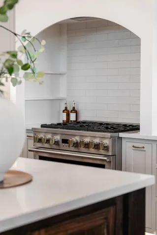 Arched alcove featuring white subway tile backsplash, professional-grade stainless steel range, and built-in shelving