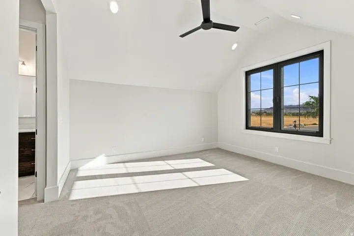 Vaulted ceiling with recessed lighting, black framed window, ceiling fan, and light-toned carpeting