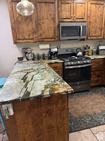 Stained wood cabinetry, patterned stone countertops, stainless steel gas range, and a built-in microwave