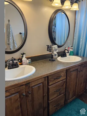 Dual oval mirrors above a spacious double vanity with wood-finish cabinetry, integrated sinks, and dark countertops
