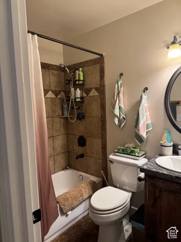 Bathtub with integrated shower, dark bronze shower fixtures, tiled shower surround, wood-finish vanity with stone-finish countertop, and circular vanity mirror