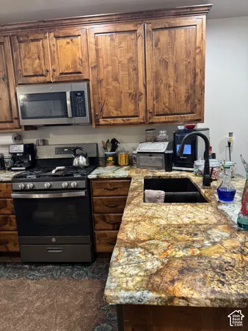 Natural wood cabinetry, stainless steel microwave, stainless steel range, mottled multi-toned countertops, and an undermount sink