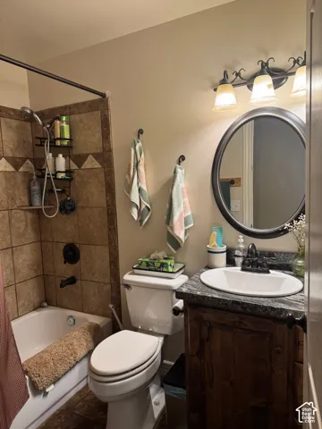 Bathtub with a tiled surround, a dark bronze shower fixture, a vanity with a dark wood-finish cabinet, a granite-finish countertop, and a round mirror